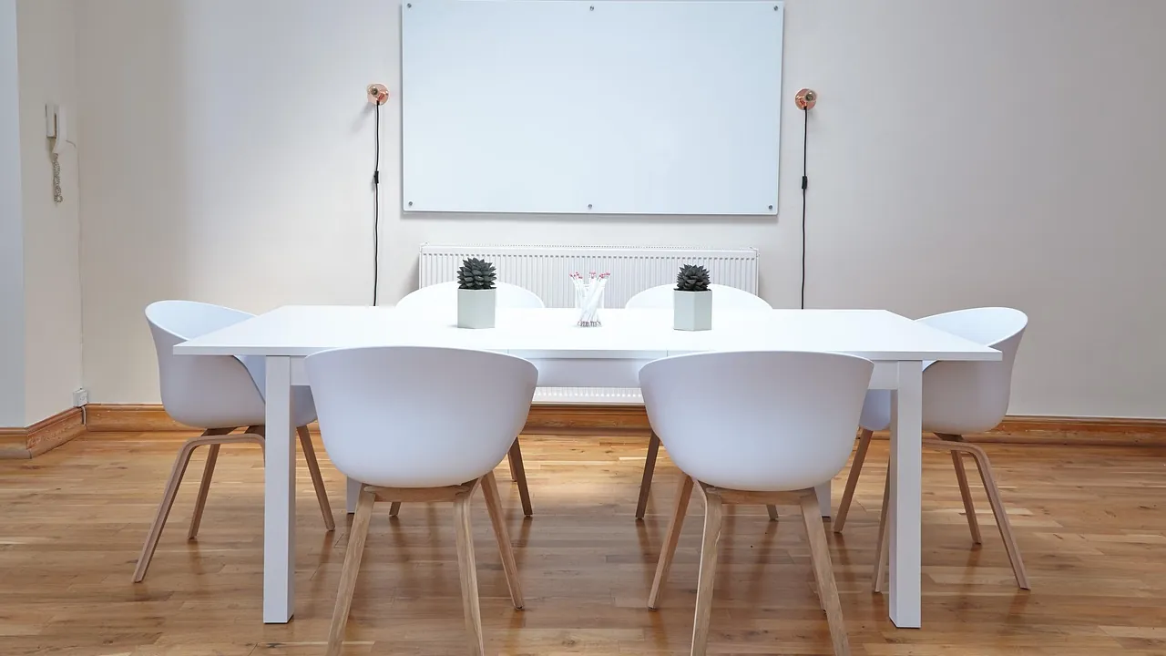 Salle de réunion claire : table blanche, chaises autour et tableau blanc