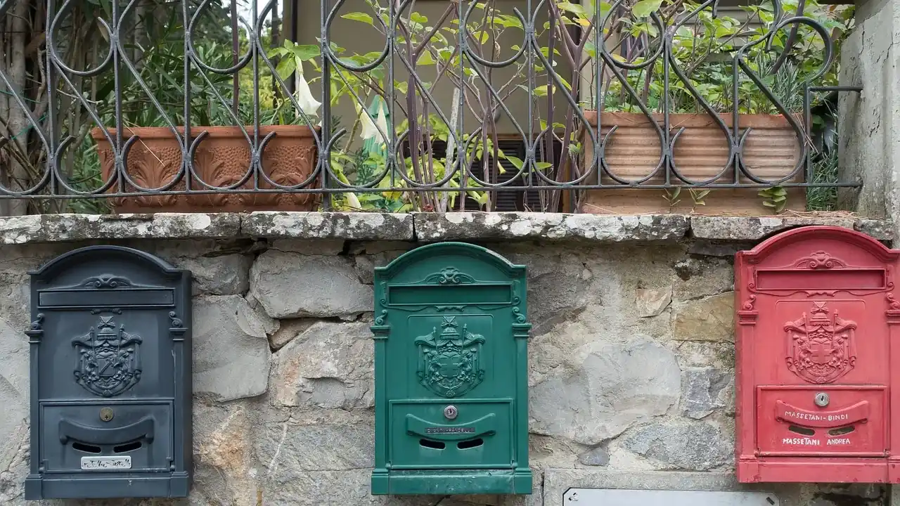 Trois boîtes aux lettres, bleu nuit, verte et rouge, sur un mur de pierre